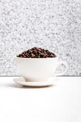 White cup with coffee seeds on granite background