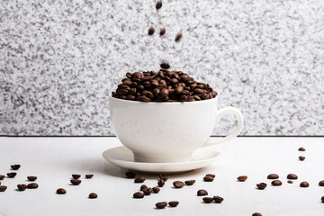 White cup with coffee seeds on granite background