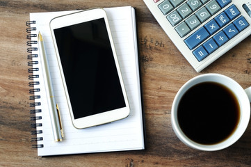 Business finance concept, smart phone, pen, notepad, coffee and calculator on a wooden table.