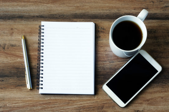 Business finance concept, blank notepad, smart phone, pen, coffee and calculator on a wooden table.