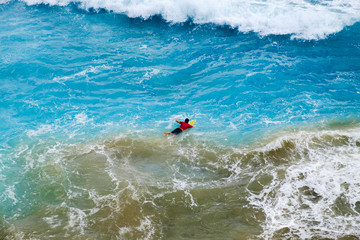 Aerial view of Surfer swimming on a board near huge blue ocean wave in Bali