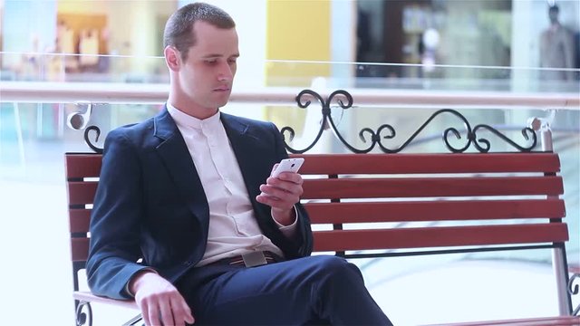 young businessman is resting sitting on a bench looking at smartphone