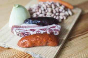 Ingredients for a spanish stew: Spanish sausages, bacon, beans, onion and carrots.