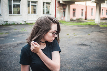 Fototapeta premium A young girl with beautiful hair and dress a black shirt waiting for friends. She straightens hair at school. The girl walk in a city. Pretty Girl. Wind develops hair