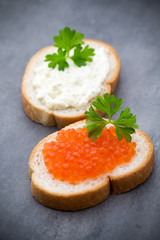 Bread with fresh cream cheese and red caviar on table.