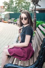 Girl in sunglasses sitting on a wooden bench in the city and waiting for friends. One girl waiting for friends.