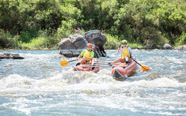 Young couple on an inflatable catamaran rowing up the stream 