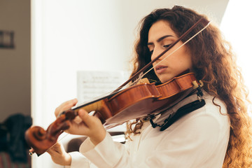 Girl playing violin. Young woman studying music alone at home in the living room with natural and...