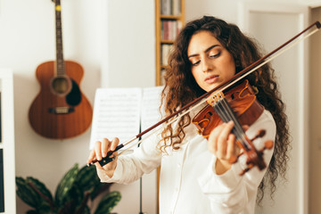 Girl playing violin. Young woman studying music alone at home in the living room with natural and...