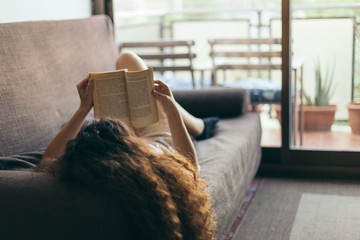 Young girl reading a book on the sofa, with curly hair and fairly dressed