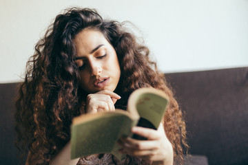 Fototapeta premium Young girl reading a book on the sofa, with curly hair and fairly dressed