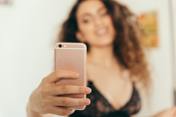 Girl sexy young and brunette taking a hot selfie alone at home and smiling with her pink phone and wearing a black bra.