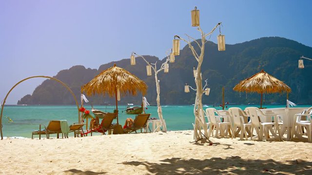 Tourists lounging in the shade of natural umbrellas at a popular resort on a tropical beach in Southeast Asia.