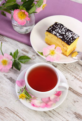 Obraz na płótnie Canvas Cup of tea with cheesecake and wild rose flower on old wooden background