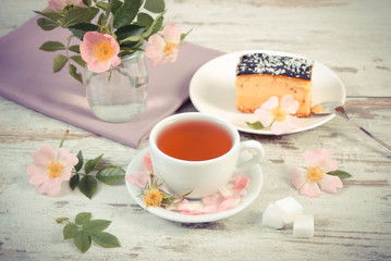 Vintage photo, Cup of tea with cheesecake and wild rose flower on old wooden background