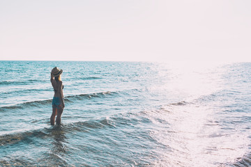 Young hipster woman standing in the sea looking at sunset