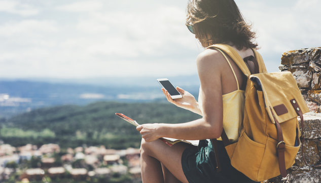 Hipster young girl with bright backpack looking at a map. View tourist traveler on background mountain, sea. Mock up for text message. Female hands using smartphone, holding gadget