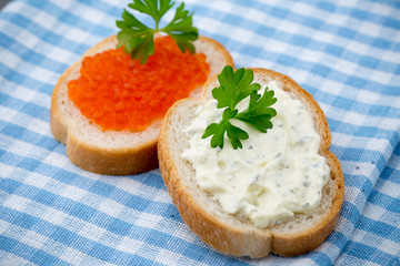 Bread with fresh cream cheese and red caviar on table.