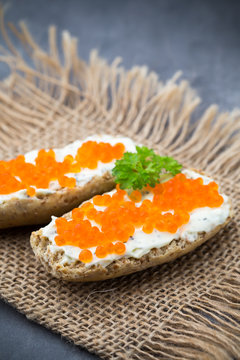 Bread with fresh cream cheese and red caviar on table.