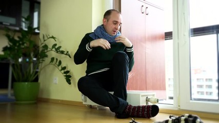 man strip warm cap and scarf sitting on heater near balcony window. - Powered by Adobe