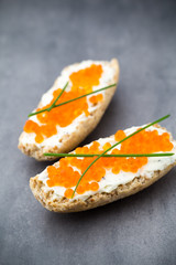 Bread with fresh cream cheese and red caviar on table.