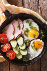 fried eggs with ham and vegetables closeup in a pan. vertical top view 
