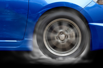 Blue car racing spinning wheel burns rubber on floor.