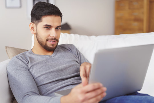 junger mann liegt gemütlich auf dem sofa und schaut auf laptop
