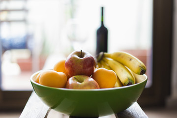 Fruit bowl full of bananas, apple, peaches and kiwi, on a table made of wood with natural light