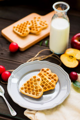 Heart-shaped waffles with apples and cherry-plums on a rustic wooden background