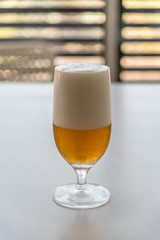 Glass of lager beer on white table against window
