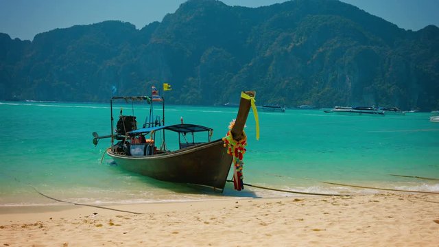 UltraHD video - Beautifully decorated longtail boat bobs in the surf as its flags flutter in the breeze on this tropical beach in Thailand.