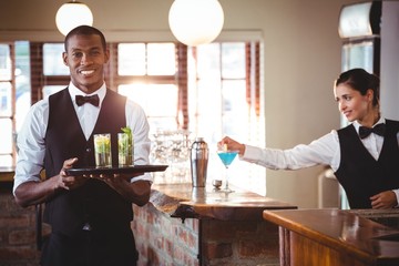 Mixed race bartender holding a serving tray with two cocktail glass