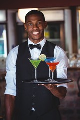 Portrait of bartender holding serving tray with cocktail glasses