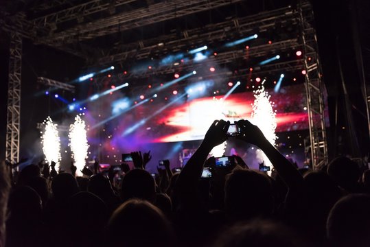 Rock concert, silhouettes of happy people raising up hands in front of bright stage lights. Space in top side.