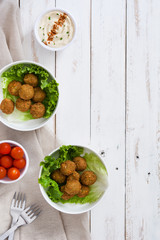 Vegetarian falafels in bowl and hummus on white wood

