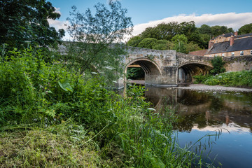 Fototapeta na wymiar Felton Old Bridge / Felton, a small village in Northumberland, with an old bridge over the River Coquet, now closed to traffic