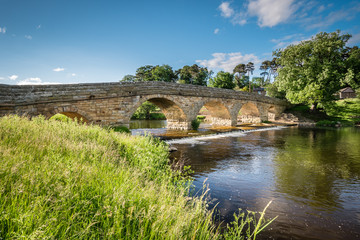 Fototapeta na wymiar Pauperhaugh Bridge and weir / Pauperhaugh Bridge just downstream from Rothbury town, on the River Coquet in Northumberland
