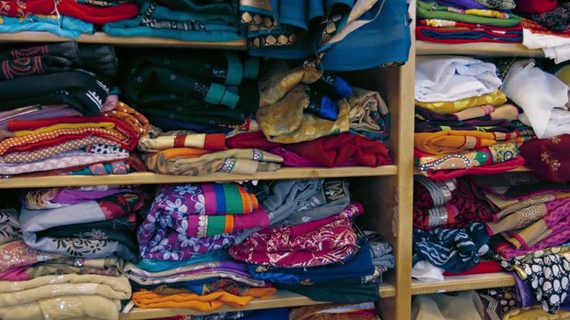 Video 3840x2160 - Rows of shelves, filled with Indian style clothing, folded and stacked on display in a streetside shop.