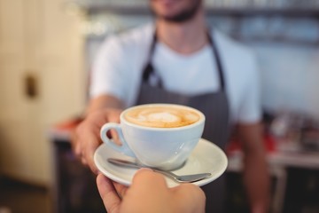 Cropped image of customer taking coffee from waiter at cafe