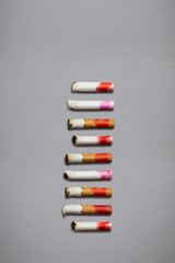 Colored butts / Creative still life of different cigarette stubs with lipstick on grey background.