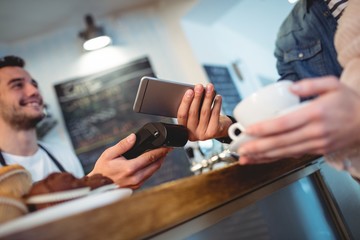 Customer with cellphone standing with barista at cafe