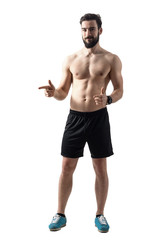 Fototapeta na wymiar Shirtless fit young athlete pointing finger and smiling at camera. Full body length portrait isolated over white studio background.
