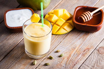 Glass of mango lassi Indian drink flavored with cardamom. Milkshake on wooden background.