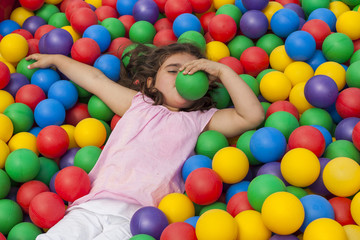Fototapeta na wymiar Girl having fun playing in a colorful plastic ball pool