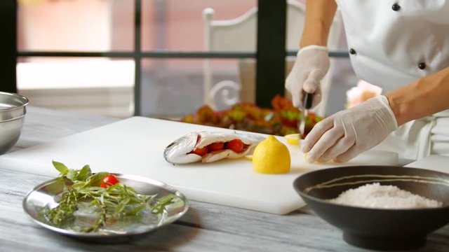 Hand with knife cuts lemon. Raw fish stuffed with tomatoes. Fresh lemon for seafood dish. Chef's new recipe.