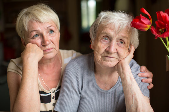An elderly woman sits thoughtfully with an adult daughter.