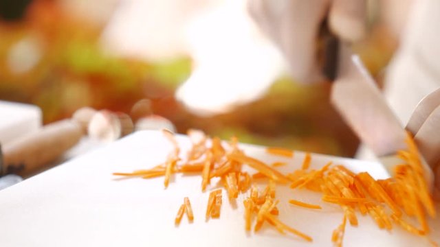 Knife quickly cuts carrot. Hand takes shredded carrot. Important ingredient for healthy salad. Fast and accurate moves.