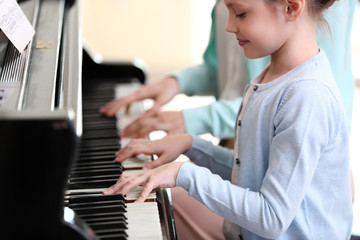 Small girl learning play piano with teacher