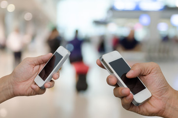 Two men holding mobile smart phone with blurred background of people at the airport.